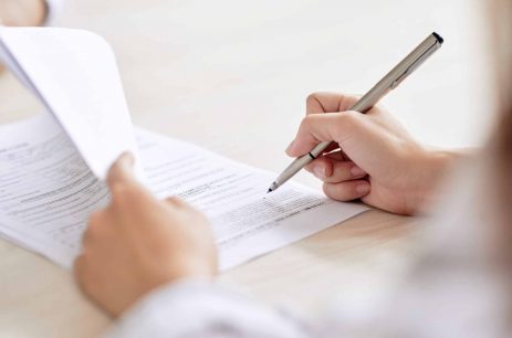 Crop person signing contract Crop shot of person with pen signing contract at desk in daylight